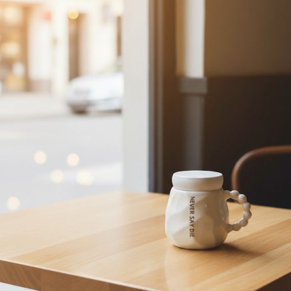 كوب خزفي أبيض بغطاء ومقبض فريد، تصميم عصري بعبارة تحفيزية “NEVER SAY DIE”